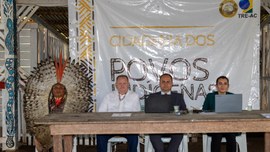 A imagem mostra quatro pessoas sentadas à frente de uma mesa. À esquerda, uma pessoa está vestid...