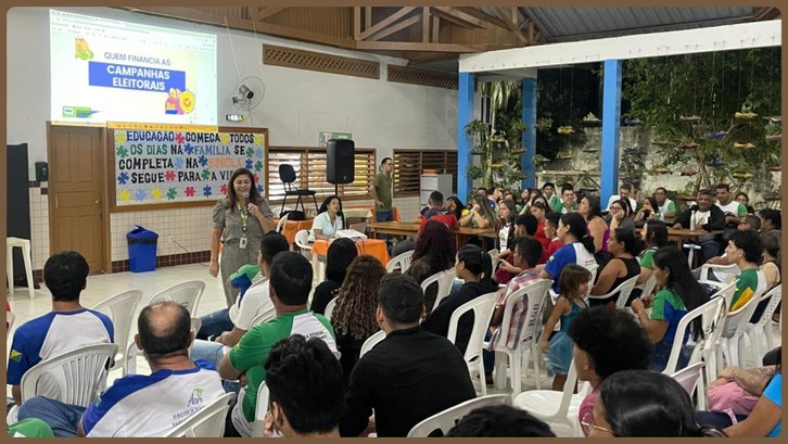 EJE realiza ação de cidadania na Escola Raimundo Gomes, em Rio Branco Uma mulher com roupa bege está a frente de vários alunos, ministrando uma palestra. Atrás dela, ...
