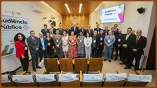 Vinte e sete (27) pessoas em pé, em um auditório no formato meia lua para uma foto oficial