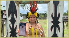 Uma (1) mulher em pé, trajando roupa tradicional dos povos originários brasileiros, segurando um...