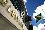 Sede do TSE. localizada na praça dos Tribunais, com céu azul e bandeira nacional ao fundo.