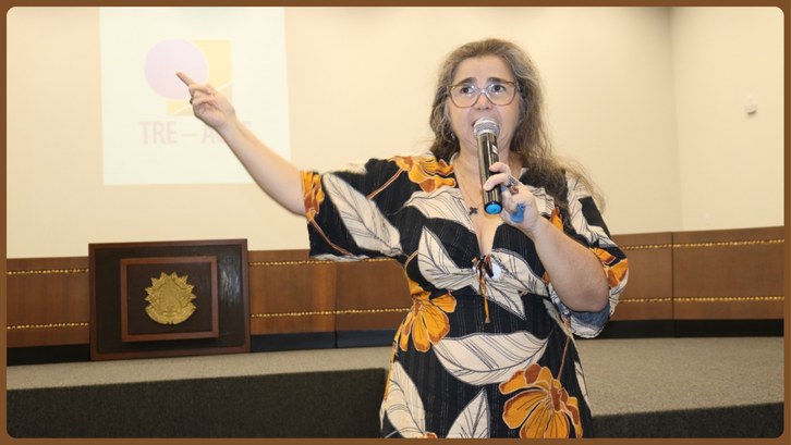 Uma (1) mulher em pé segurando um (1) microfone preto em um (1) auditório