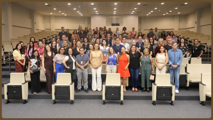 TRE-AC celebra Dia das Mães com bate-papo especial Um grande grupo de pessoas está reunido para uma foto coletiva em um auditório. Elas estão distr...