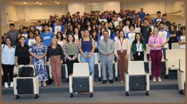 Foto de grupo tirada em auditório, com estudantes e profissionais distribuídos em pé nas fileira...